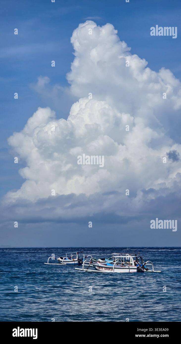 Barche tradizionali che galleggiano sulle calme acque oceaniche con una formazione di nuvole che si innalza sopra l'orizzonte, creando un paesaggio marino tropicale e destinazione di viaggio - Immagine stock catturata con smartphone