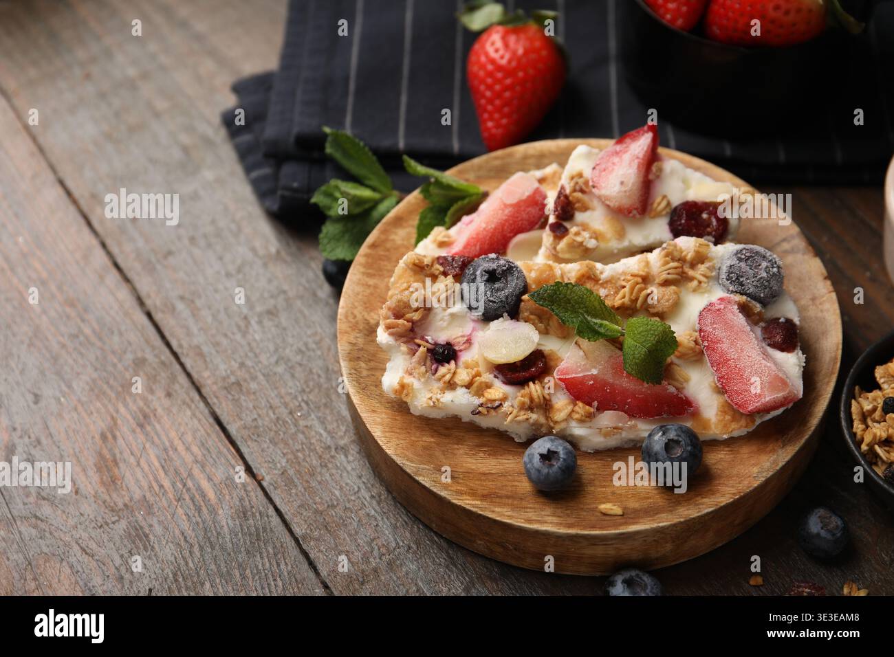 Pezzi di gustosa corteccia di yogurt con frutti di bosco, menta e muesli su tavola di legno, primo piano. Spazio per il testo Foto Stock