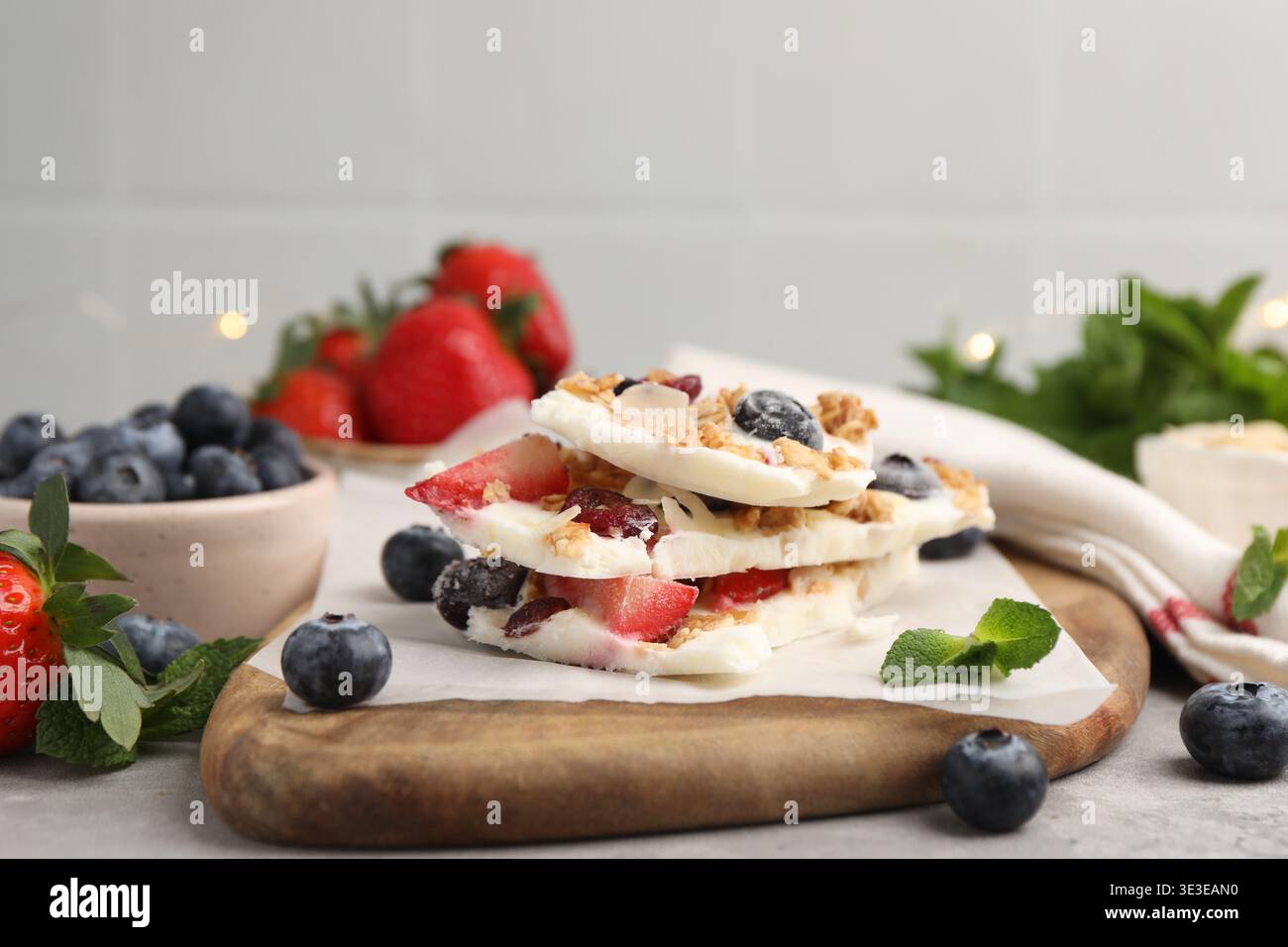 Pezzi di gustosa corteccia di yogurt con frutti di bosco, muesli e menta sul tavolo grigio, primo piano Foto Stock