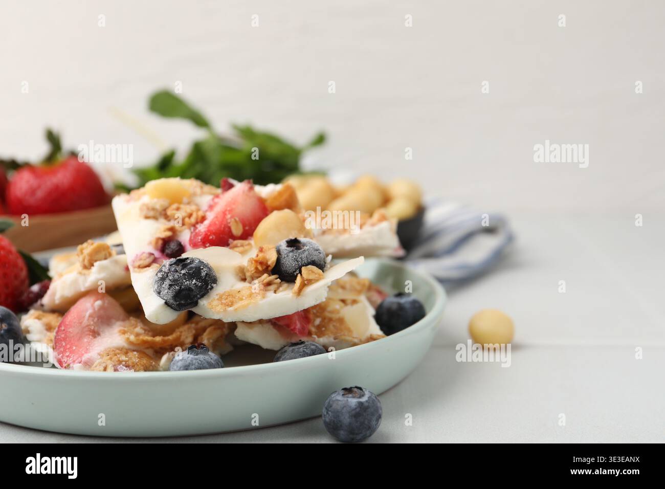 Pezzi di gustosa corteccia di yogurt con frutti di bosco e muesli su un tavolo piastrellato leggero, primo piano. Spazio per il testo Foto Stock