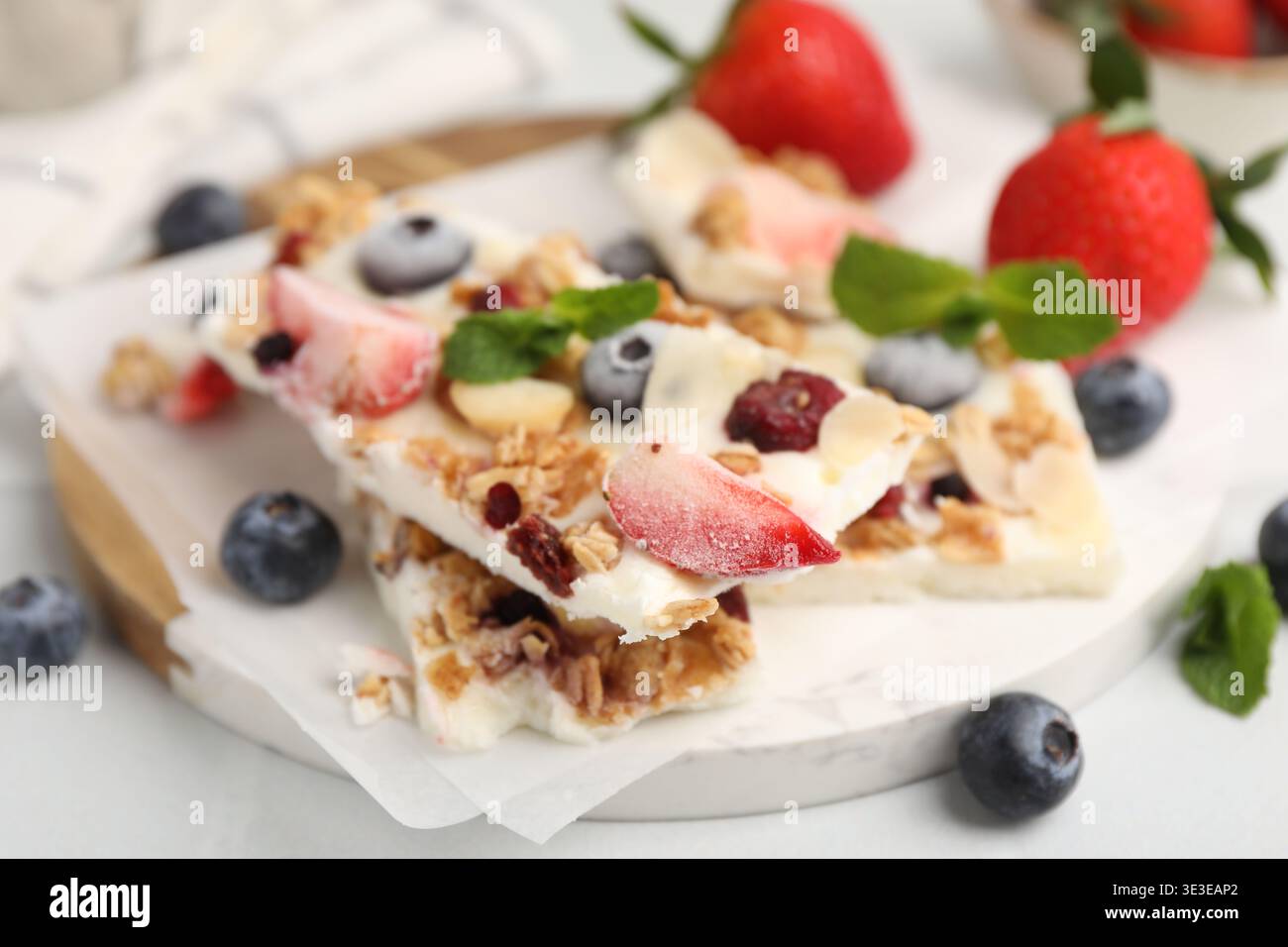 Pezzi di gustosa corteccia di yogurt con frutti di bosco, muesli e menta sul tavolo leggero, primo piano Foto Stock