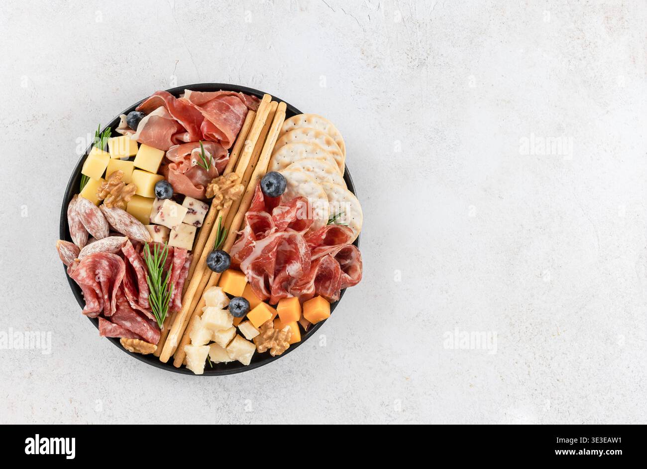 Tagliere di salumi con formaggi assortiti, affettati, cracker, noci su sfondo bianco. Vista dall'alto. Copia spazio Foto Stock