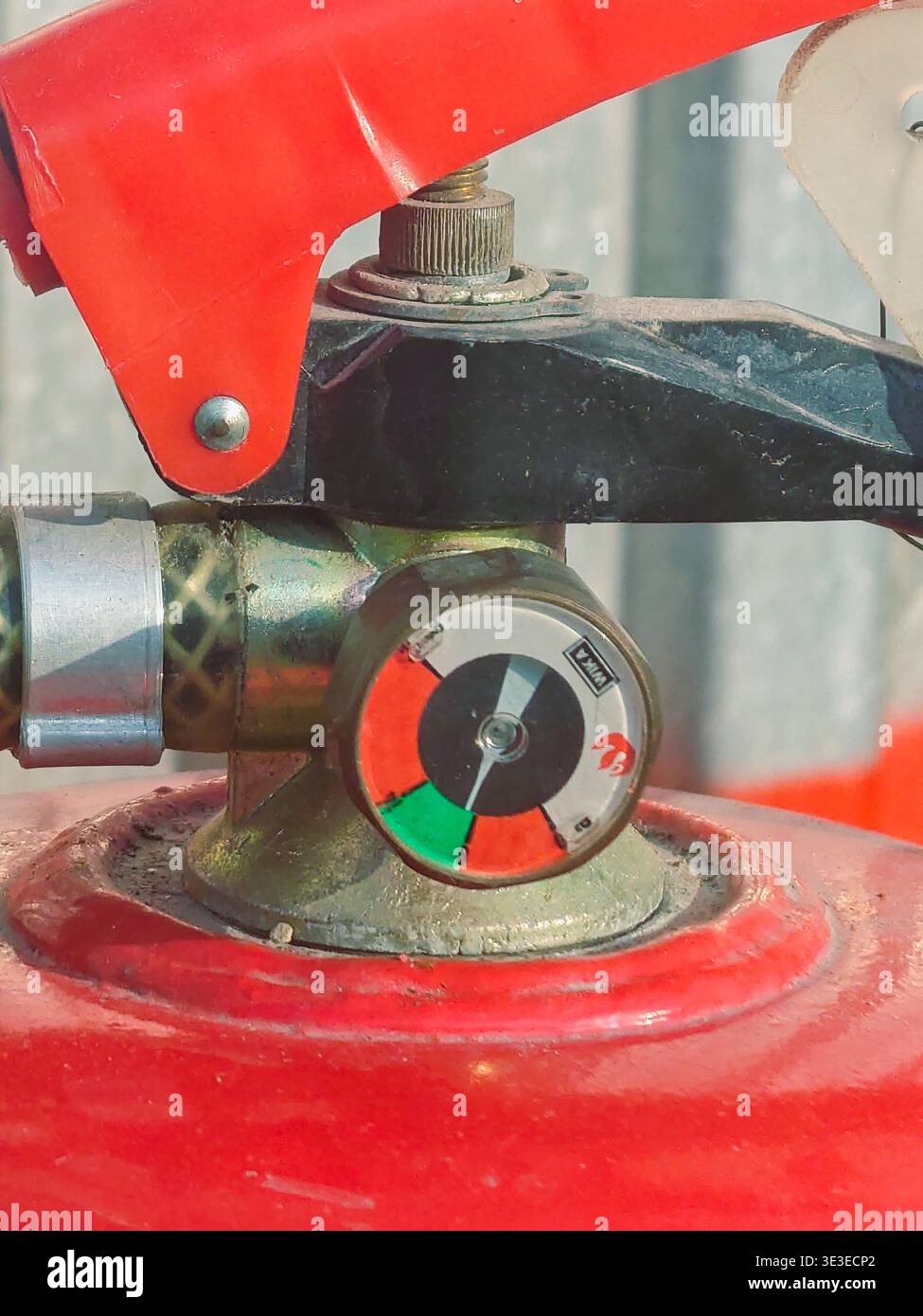 Una fotografia macro dettagliata del manometro e della maniglia di azionamento di un estintore rosso. L'indicatore indica che il dispositivo è pressurizzato e r Foto Stock