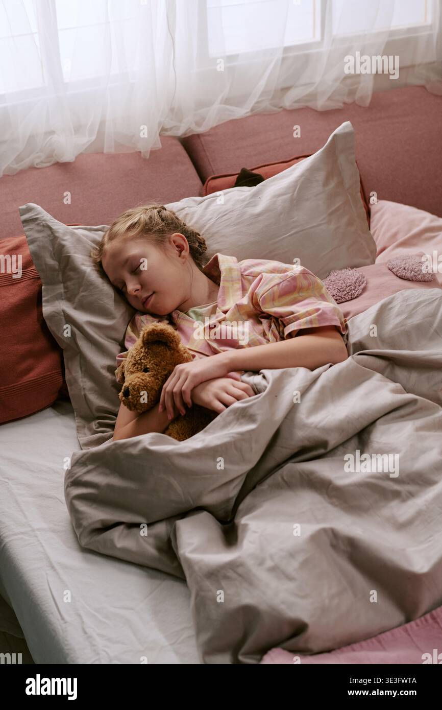 Ragazza che dorme tranquillamente a letto mentre abbraccia peluche Toy Bear Foto Stock