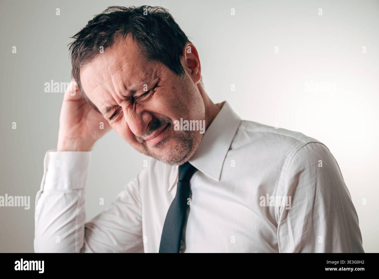Uomo d'affari che soffre con la mano premuta sulla fronte, occhi chiusi in profonda concentrazione, cercando di ricordare qualcosa di importante. Concetto per dimenticanze Foto Stock