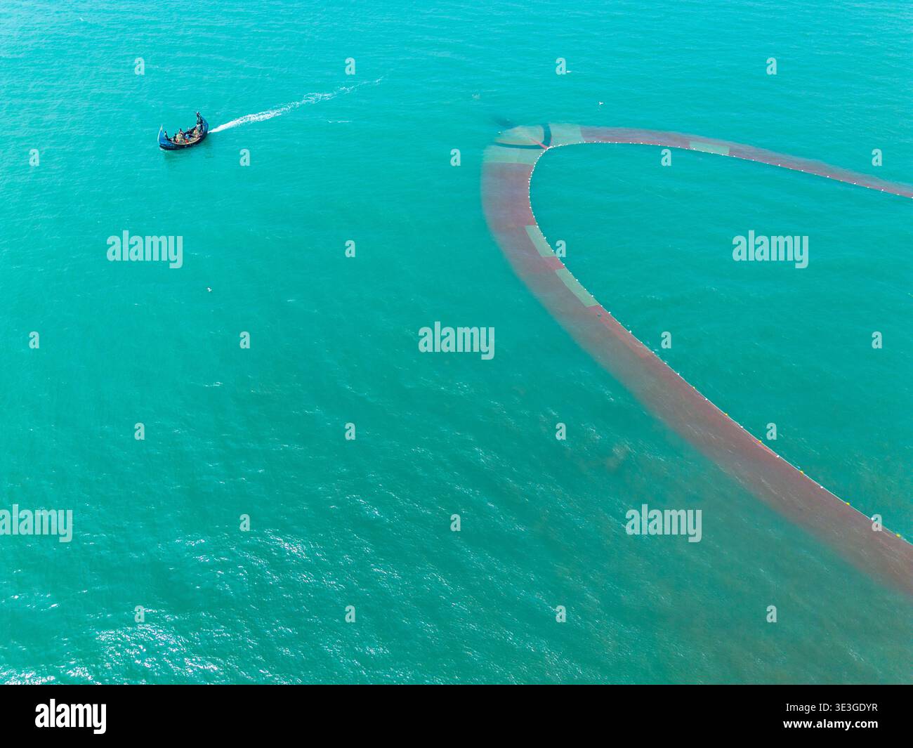 Cox's Bazar, Bangladesh - 10 marzo 2026: Veduta aerea di una barca da pesca che taglia un sentiero attraverso le tranquille acque turchesi, lasciando un sentiero di Foto Stock