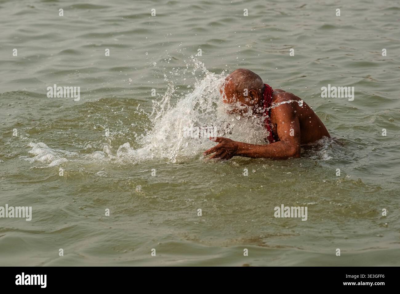 Un uomo anziano fa un bagno rituale spruzzando acqua sulla testa nel fiume Gange a un ghat a Varanasi. Foto Stock