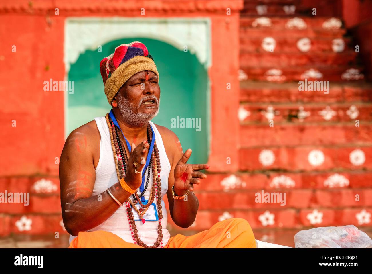 Un ritratto di un uomo in abito tradizionale che canta durante una cerimonia in un ghat a Varanasi, con il fiume Gange in lontananza. Foto Stock