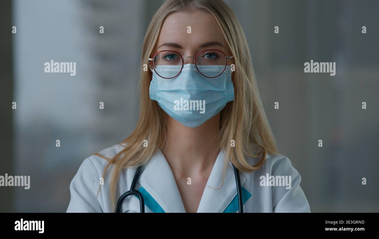 Ritratto medico caucasico donna in faccia maschera medica protettiva guardando la macchina fotografica in ospedale clinica ragazza pandemica lavoro medico lavoro Foto Stock