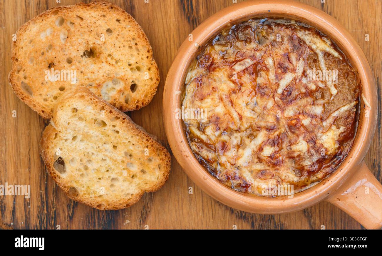 Tradizionale zuppa francese di cipolle con baguette e formaggio gruyere (emmental, comte o beaufort) in ciotola di ceramica su fondo di legno. Messa a fuoco selettiva Foto Stock