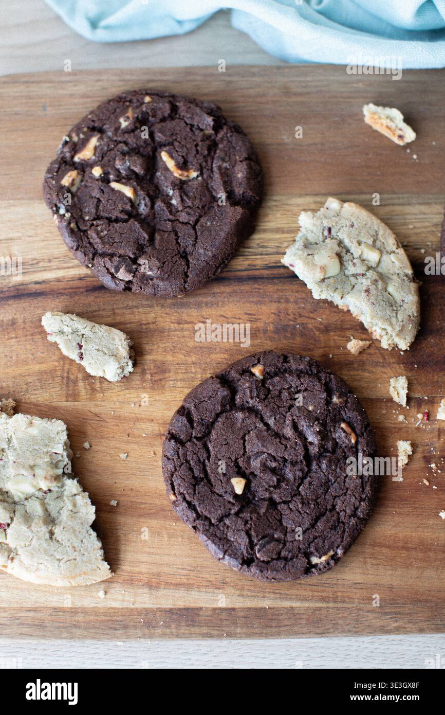 biscotti appena sfornati sparsi su un tagliere di legno. La collezione comprende biscotti fondenti con due gocce di cioccolato Foto Stock