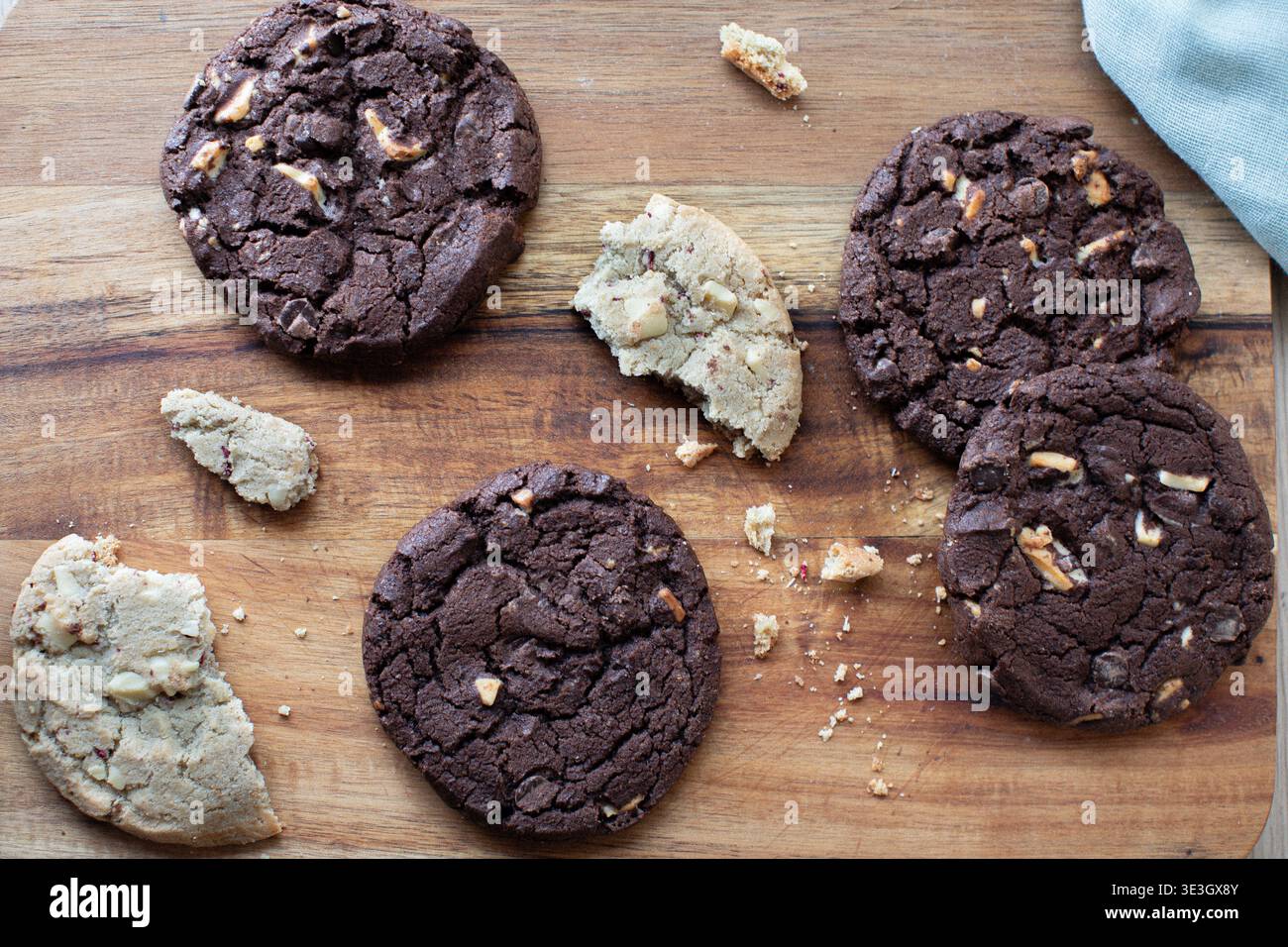 biscotti appena sfornati sparsi su un tagliere di legno. La collezione comprende biscotti fondenti con due gocce di cioccolato Foto Stock