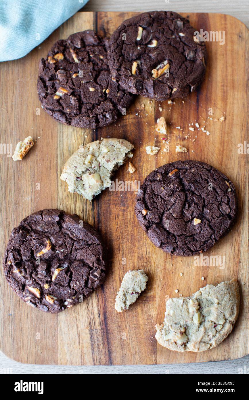 biscotti appena sfornati sparsi su un tagliere di legno. La collezione comprende biscotti fondenti con due gocce di cioccolato Foto Stock