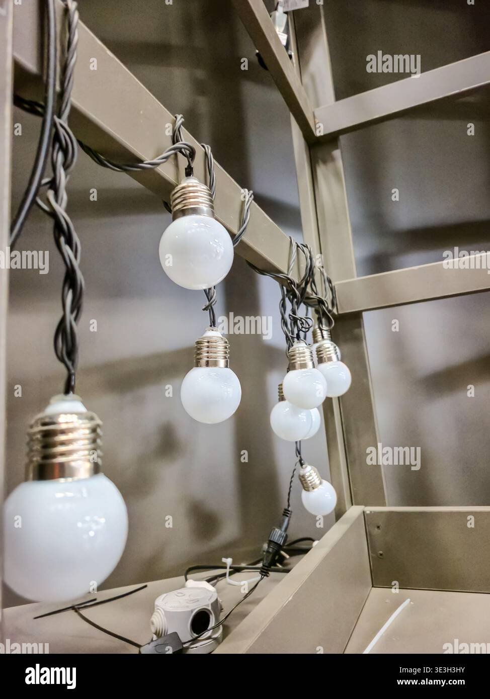 Una serie di piccole lampadine bianche rotonde su un cavo scuro sono sospese da una struttura in metallo abbronzato, suggerendo l'illuminazione per esterni o eventi Foto Stock