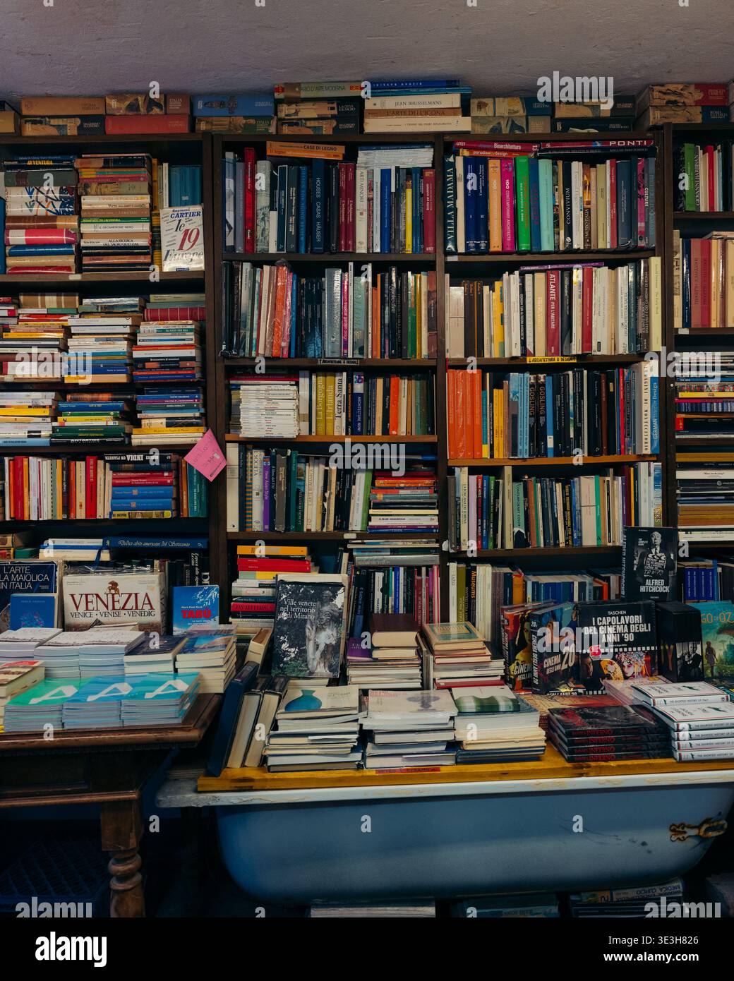 Venezia, Italia - 1 maggio 2025: Vista di una libreria piena di colorate spine di libri, impilata su scaffali e traboccante di vasca, creando Foto Stock