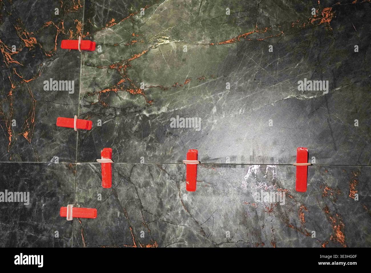 Vista dettagliata della superficie in marmo verde con distanziali rossi per l'allineamento delle giunzioni durante il processo di incollaggio Foto Stock