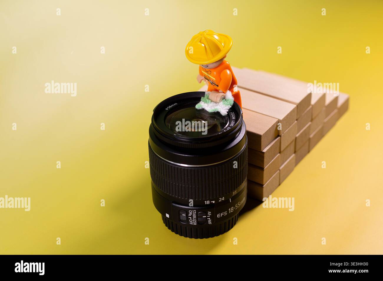 Immagine concettuale creativa di piccole statuette giocattolo che eseguono la pulizia e la manutenzione dell'obiettivo della fotocamera. Foto Stock