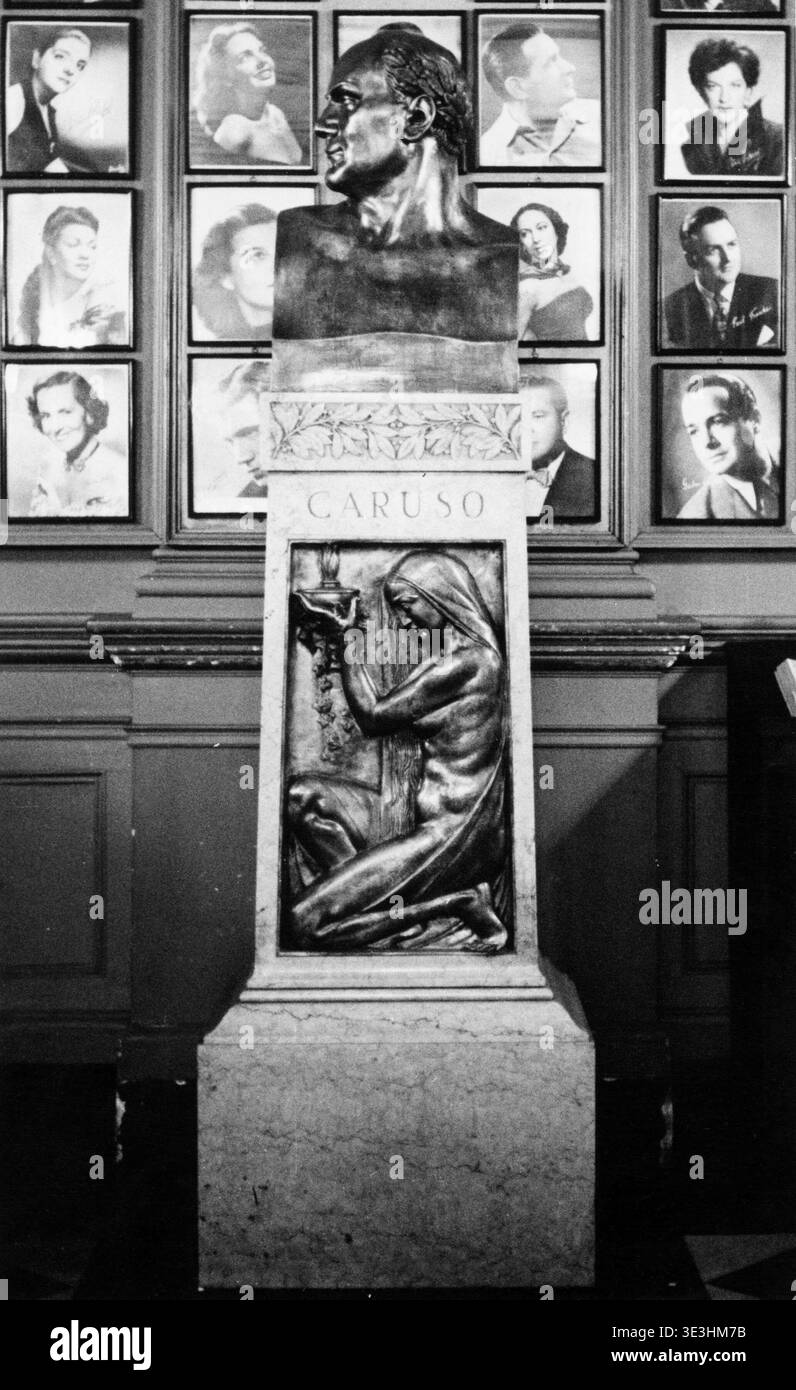 Questa straordinaria fotografia in bianco e nero degli anni '1940 cattura un busto del cantante d'opera Enrico Caruso, in mostra con il suo nome scolpito sotto e una scultura in bassorilievo di una figura inginocchiata. Il busto è circondato da ritratti incorniciati di vari individui disposti su un muro, probabilmente figure di spicco dell'epoca. Foto Stock