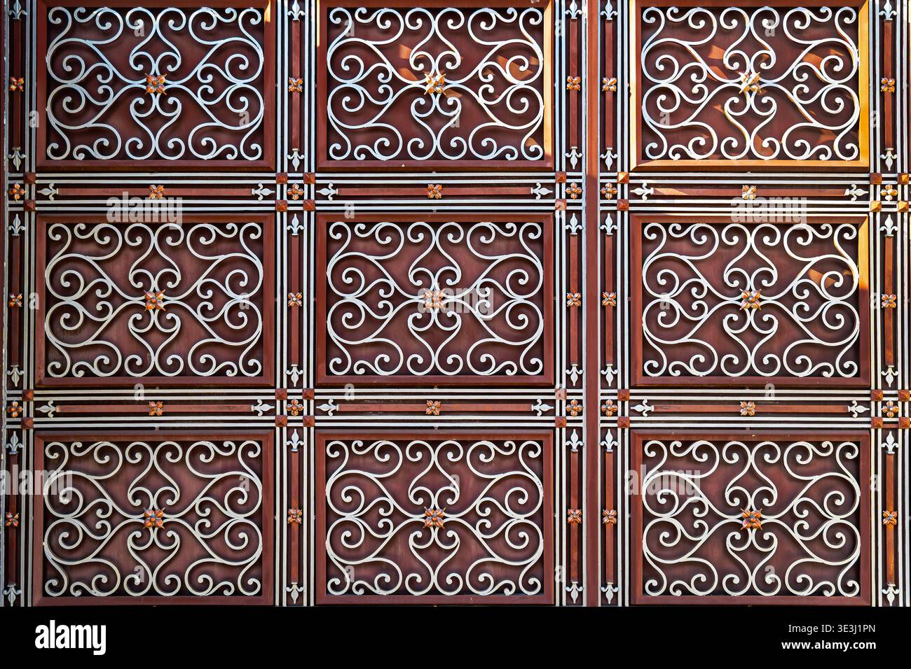 Sfondo decorato in ferro battuto. Primo piano di un cancello in ferro battuto decorato con un motivo floreale ricorrente, tonalità rosse ricche e simmetriche Foto Stock