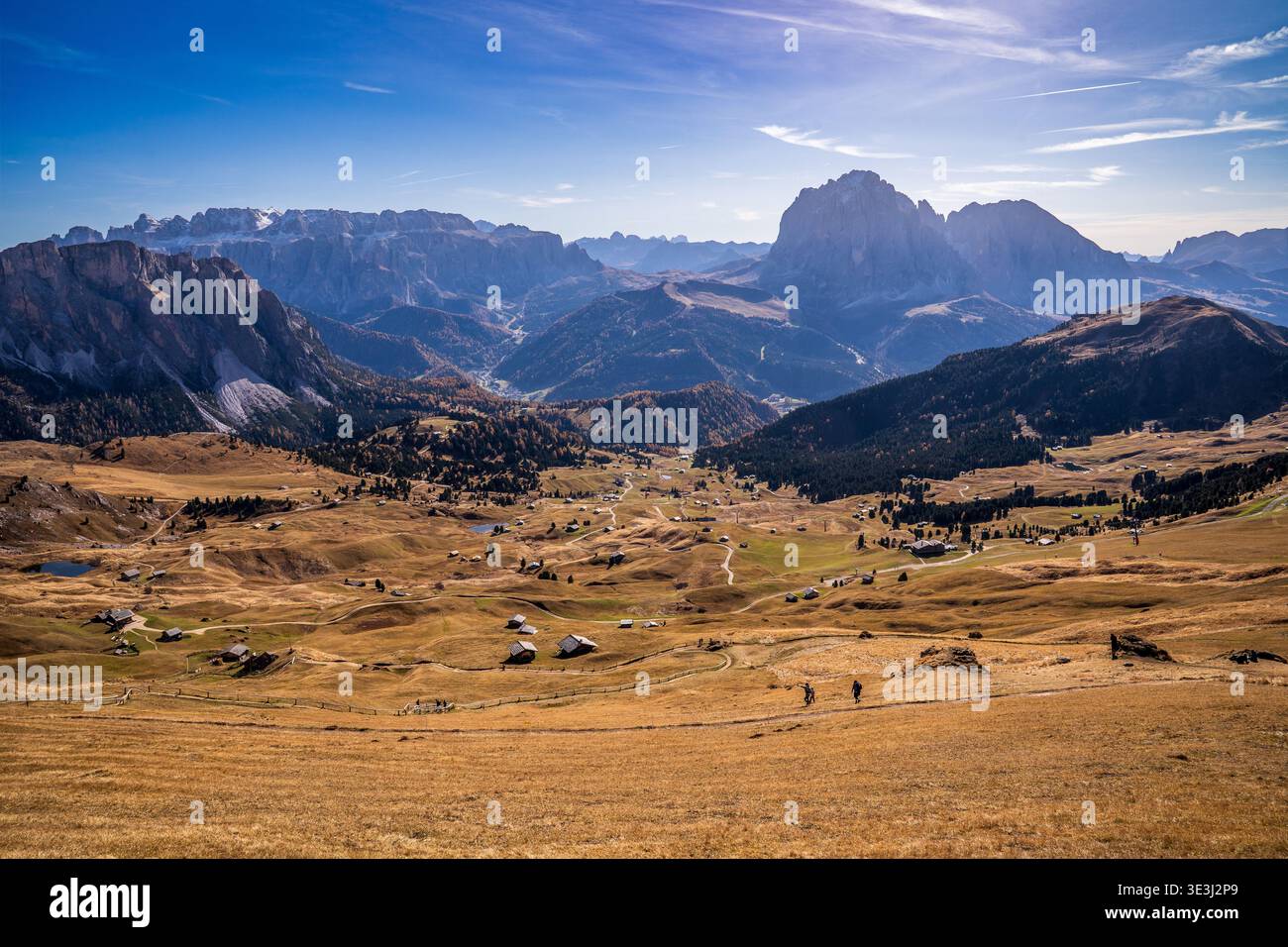 Vista panoramica autunnale delle Dolomiti da Seceda. Prati dorati con capanne di legno, escursionisti su sentieri e le maestose vette del Sassolungo e del Sella Foto Stock