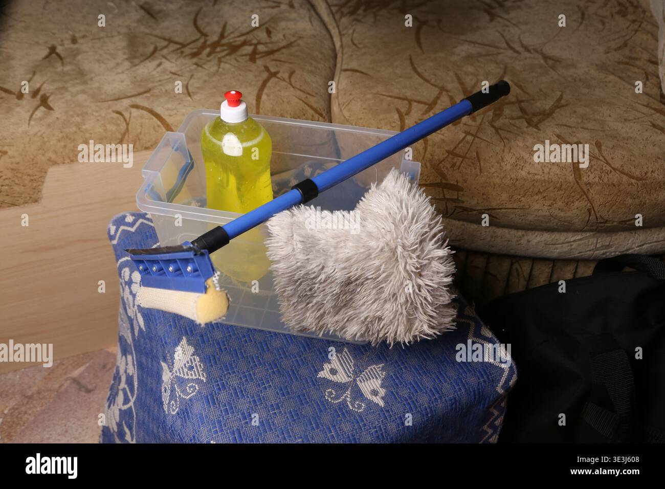 Un contenitore contiene prodotti per la pulizia, tra cui una bottiglia di detergente liquido, una spugna per la pulizia e un panno antipolvere. Gli articoli sono organizzati e pronti per la pulizia in soggiorno Foto Stock