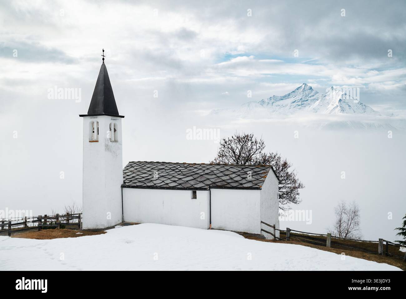 Vecchia chiesa nel paesaggio invernale, con montagne innevate che si affacciano su un mare di nuvole, Valle d'Aosta, Italia Foto Stock