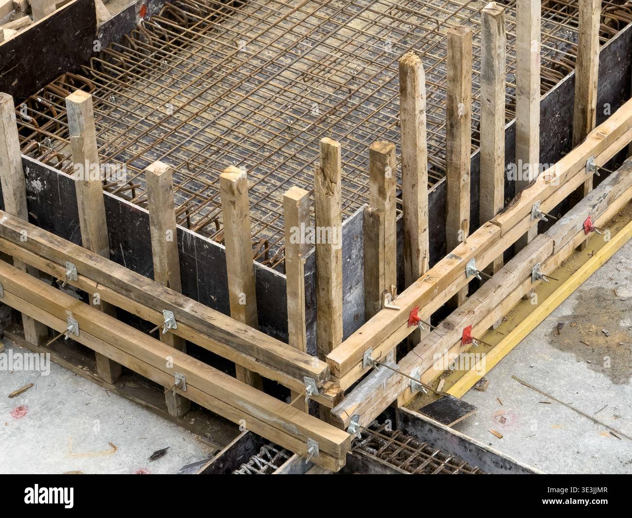 Vista delle tavole di legno grezzo e dei tondini in metallo formano un motivo geometrico netto contro il calcestruzzo grigio, uno studio sulle trame e la preparazione industriale, İs Foto Stock