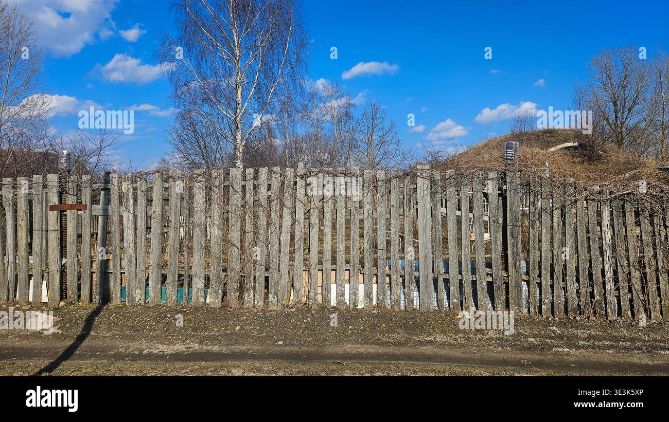 Vecchia recinzione rurale in legno con viti asciutte e paesaggio di campagna blu Foto Stock