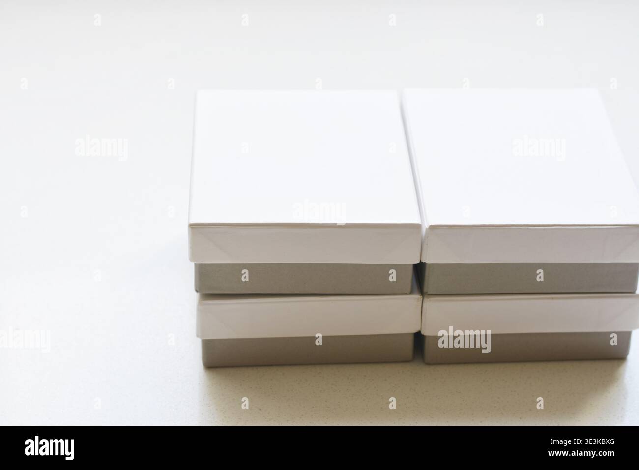 Immagine ad alta risoluzione di caselle quadrate bianche con basi grigie impilate ordinatamente su un tavolo bianco. Composizione minimalista che rappresenta l'imballaggio, il branding, Foto Stock