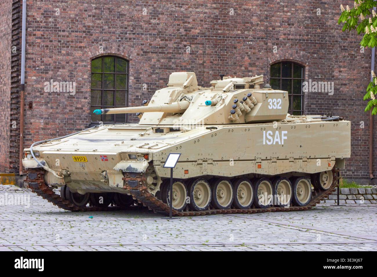 Un veicolo da combattimento della fanteria norvegese CV90 esposto all'aperto di fronte a uno storico edificio industriale in mattoni rossi con finestre ad arco. Il deserto Foto Stock