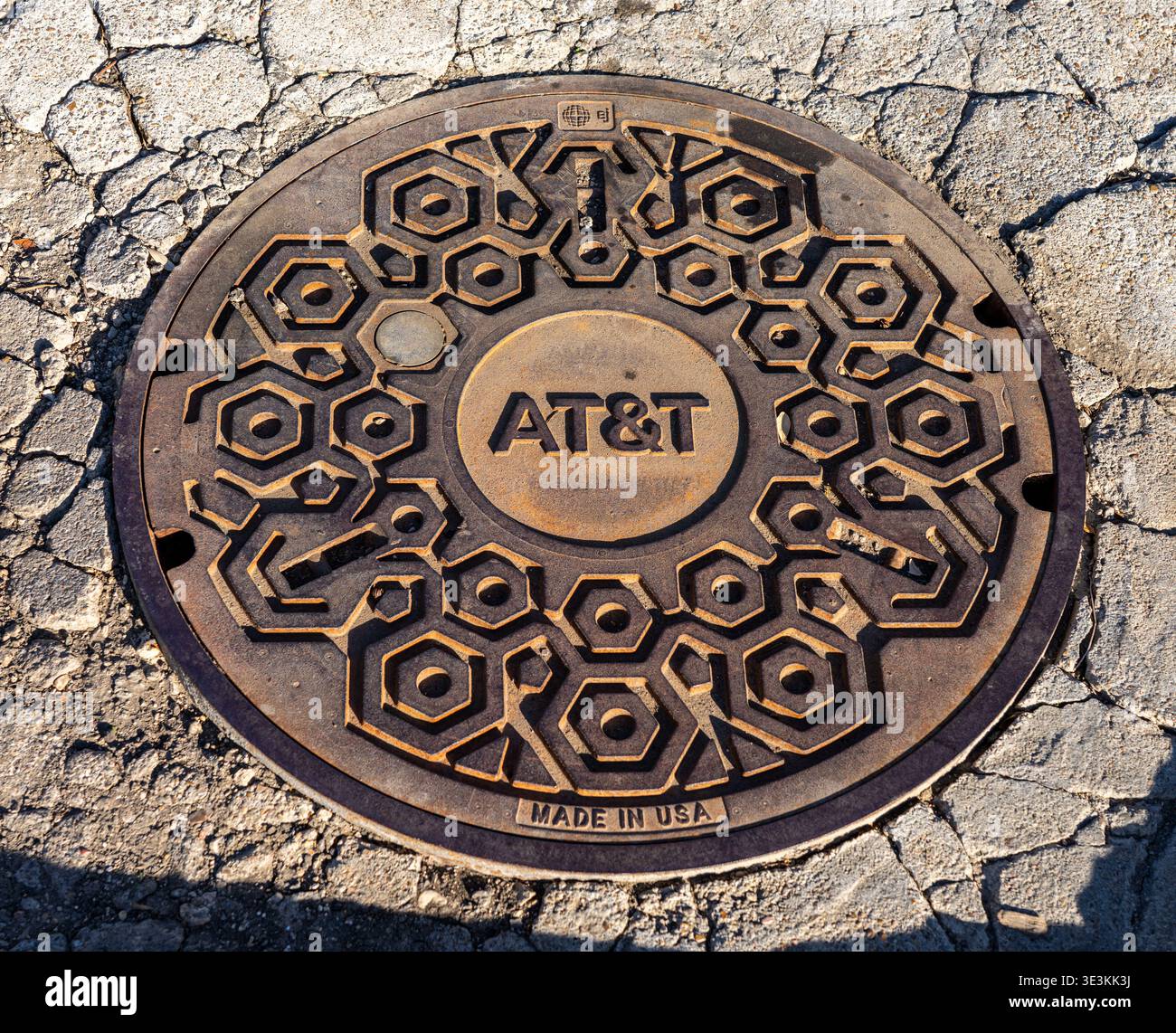 Una copertura per tombini poggia su un marciapiede incrinato a Georgetown, Texas. La copertina mostra il logo AT&T e un design geometrico unico. Foto Stock