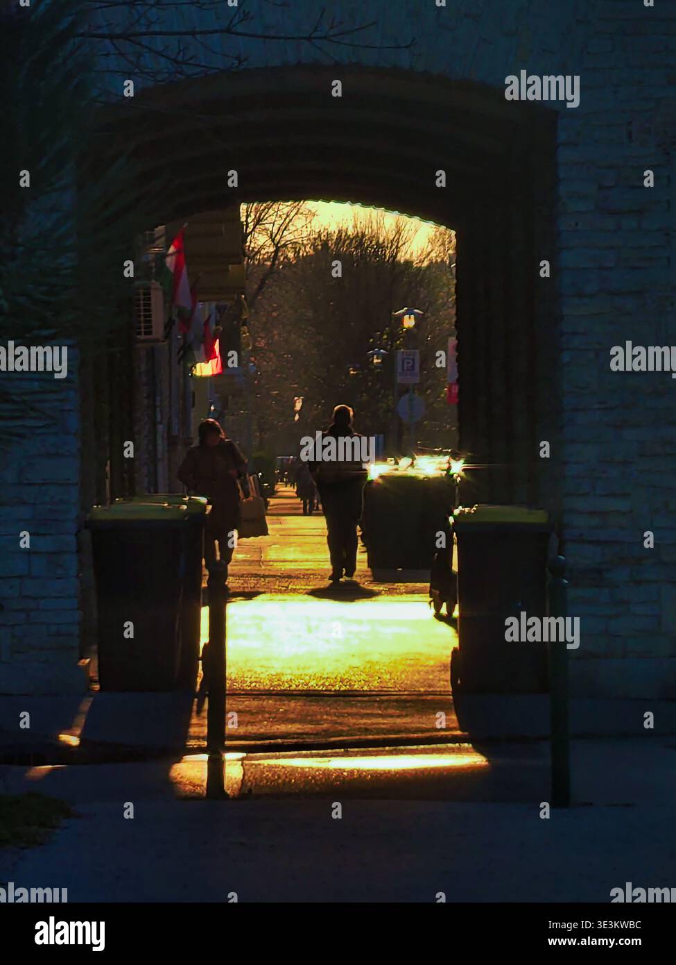 Una fotografia verticale del paesaggio urbano scattata dall'interno di un tunnel di pietra scura che guarda verso una strada soleggiata di Budapest. Pedestri sagomati Foto Stock