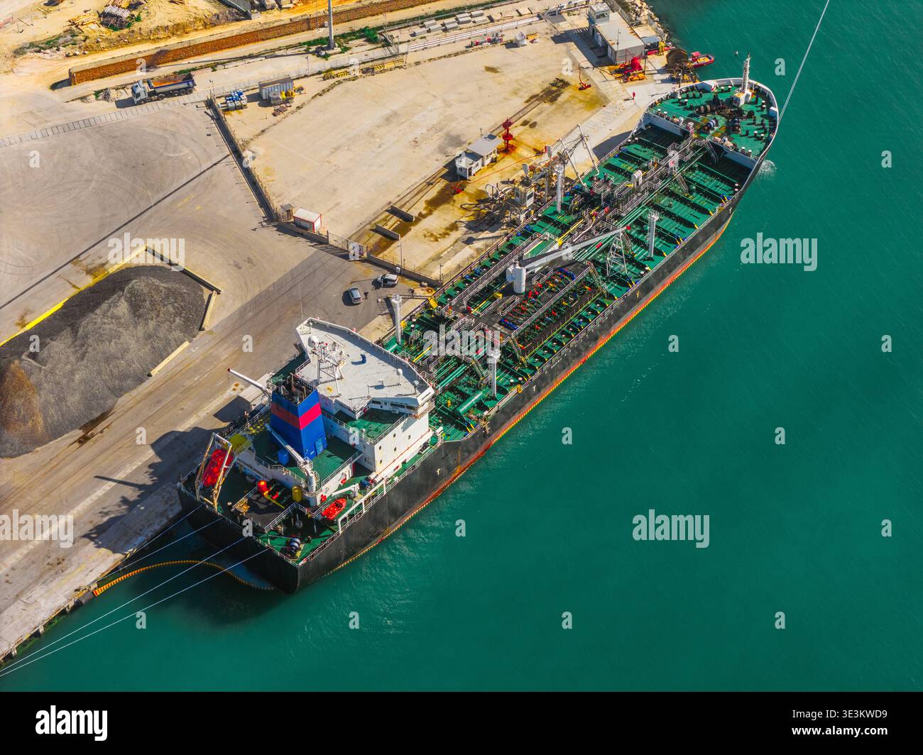 La vista aerea di un'enorme nave cisterna, un titano di acciaio e colore, contrasta con le tranquille acque turchesi del porto, ancorate al molo industriale, o. Foto Stock