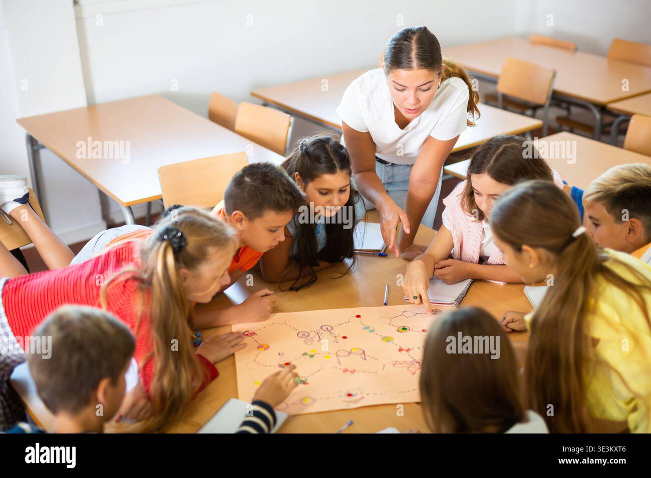 I bambini e l'insegnante femminile giocano insieme un gioco da tavolo educativo in classe a scuola Foto Stock