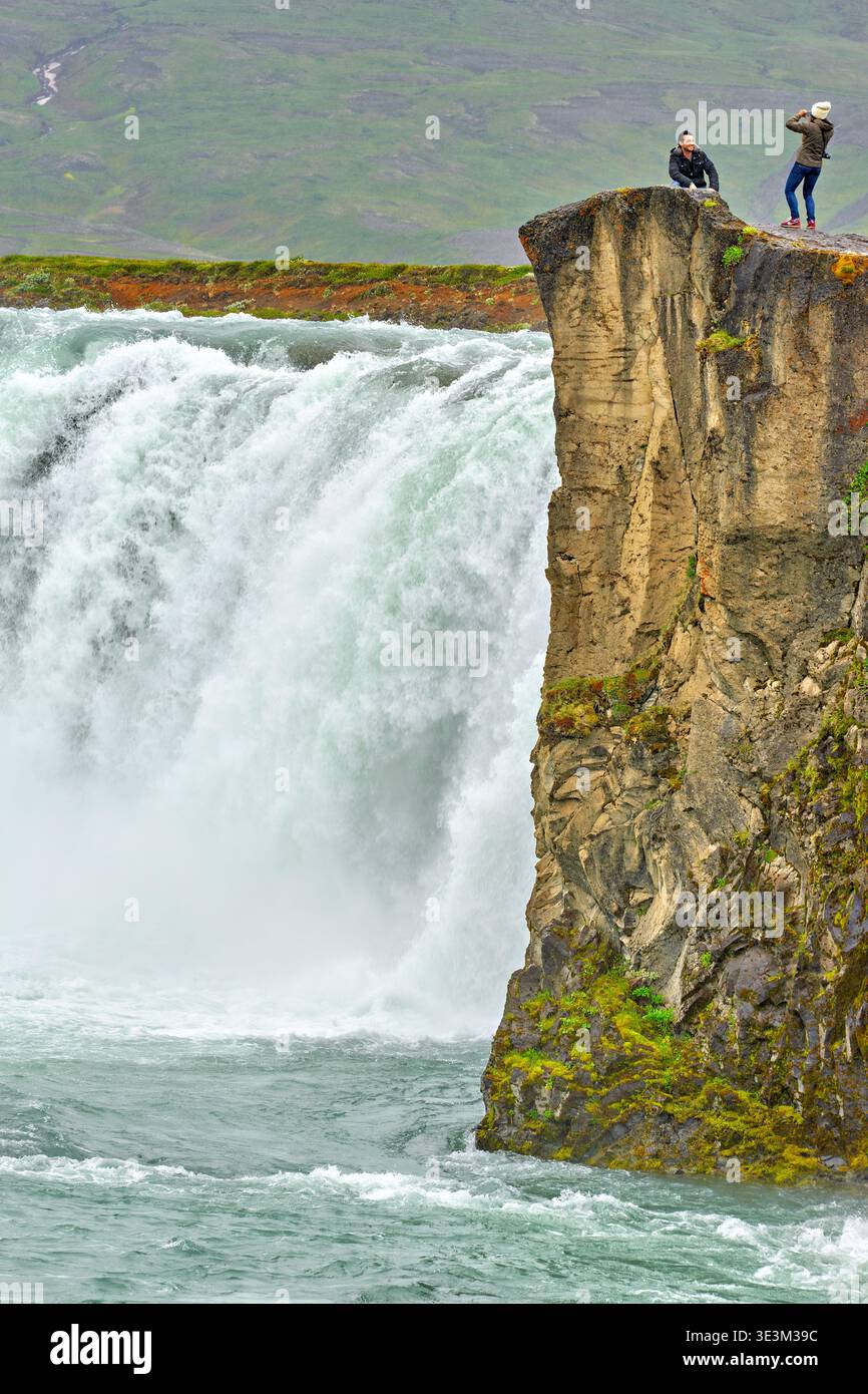 I visitatori guardano oltre il bordo della cascata Godafoss in Islanda. L'acqua scorre potente, creando una scena possente in natura. Foto Stock