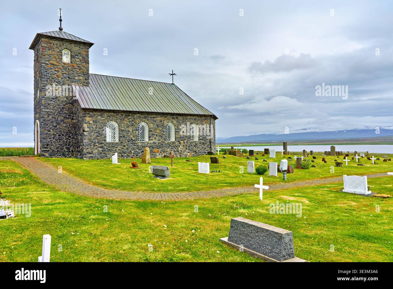 La chiesa di Tyngeyraklausturskirkja si trova vicino a un cimitero sulla costa. Le nuvole coprono il cielo mentre i visitatori esplorano la zona. Foto Stock