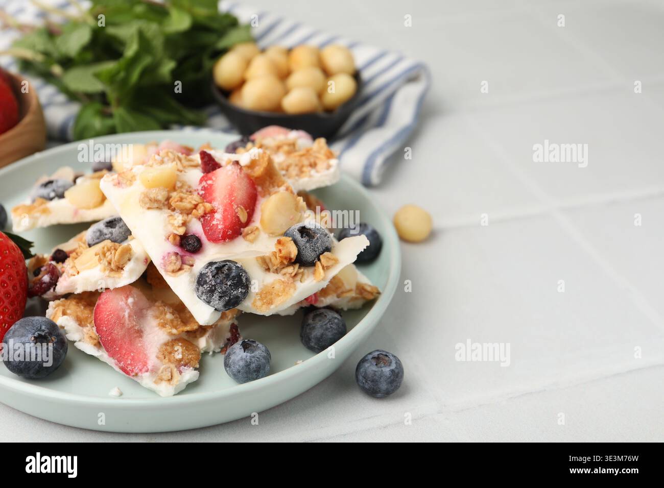 Pezzi di gustosa corteccia di yogurt con frutti di bosco e muesli su un tavolo piastrellato leggero, primo piano. Spazio per il testo Foto Stock