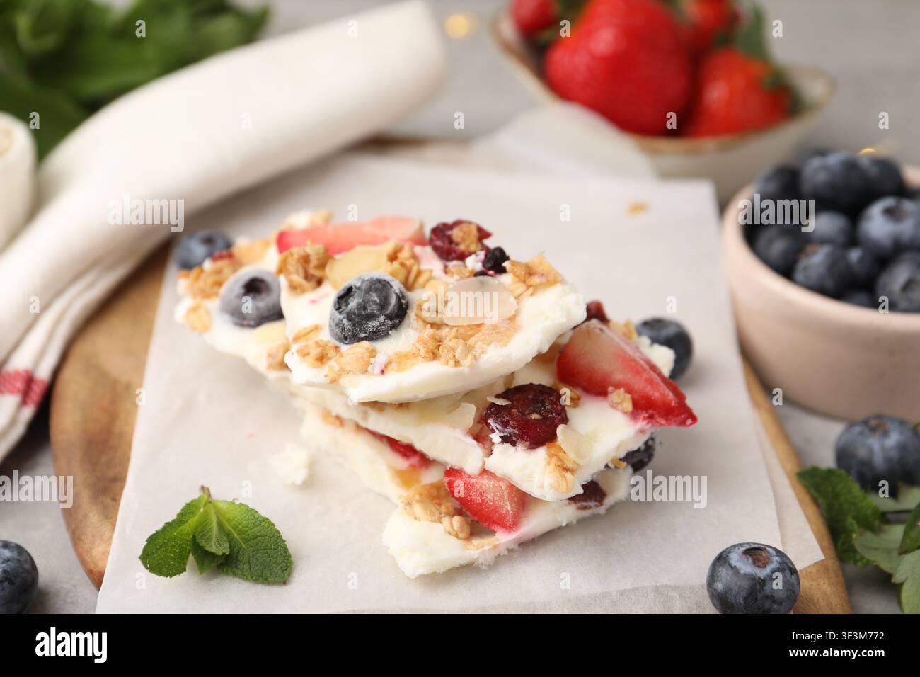 Pezzi di gustosa corteccia di yogurt con frutti di bosco, muesli e menta sul tavolo grigio, primo piano Foto Stock