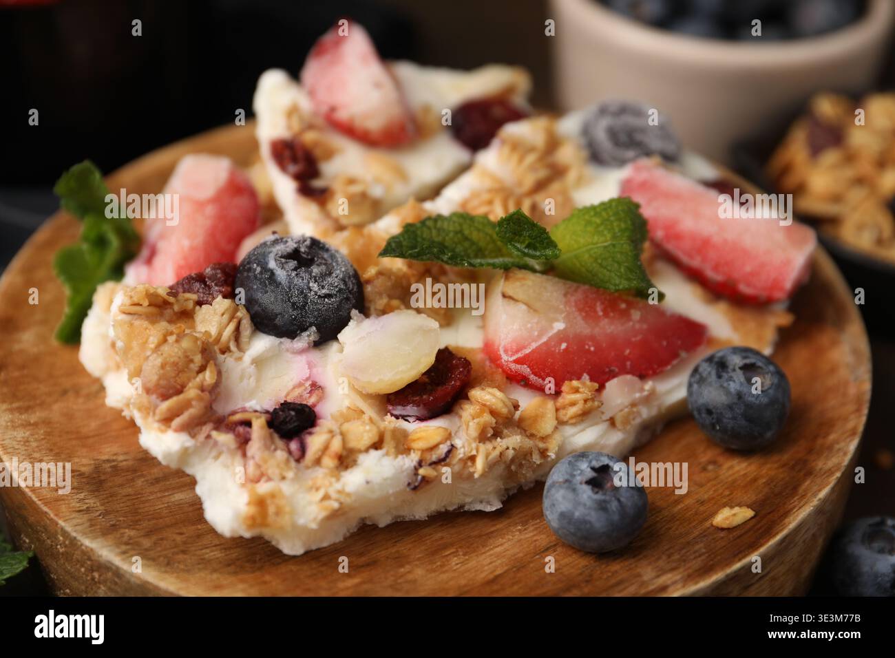 Pezzi di gustosa corteccia di yogurt con frutti di bosco, menta e muesli sul tavolo, primo piano Foto Stock