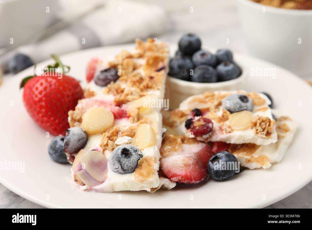 Pezzi di gustosa corteccia di yogurt con frutti di bosco, scaglie di mandorle e muesli sul tavolo, primo piano Foto Stock