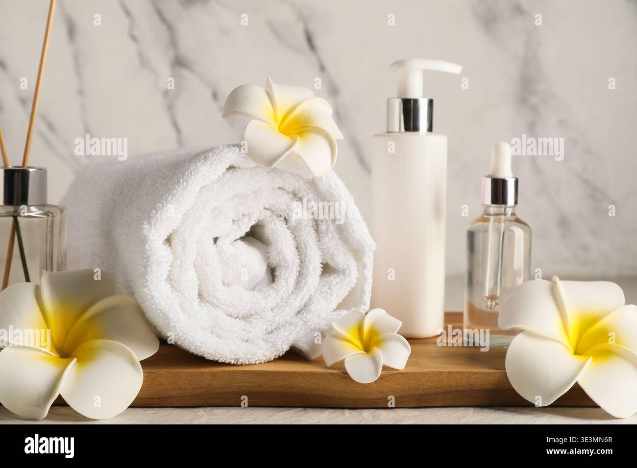 Asciugamano, fiori di plumeria e bottiglie di prodotti cosmetici su un tavolo grunge bianco vicino alla parete di marmo, primo piano Foto Stock