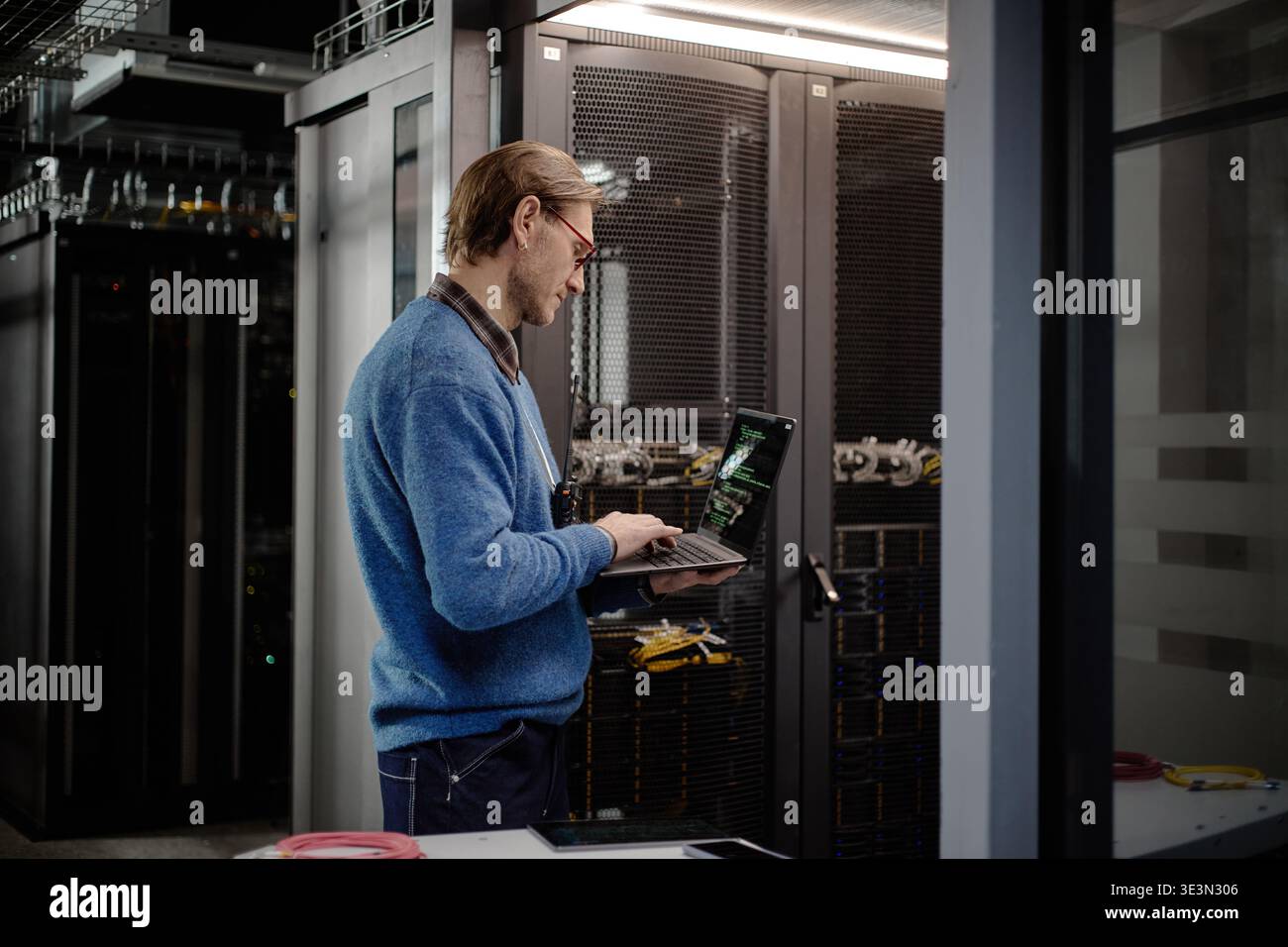 Uomo caucasico di mezza età che utilizza un laptop durante il monitoraggio delle apparecchiature della sala server Foto Stock