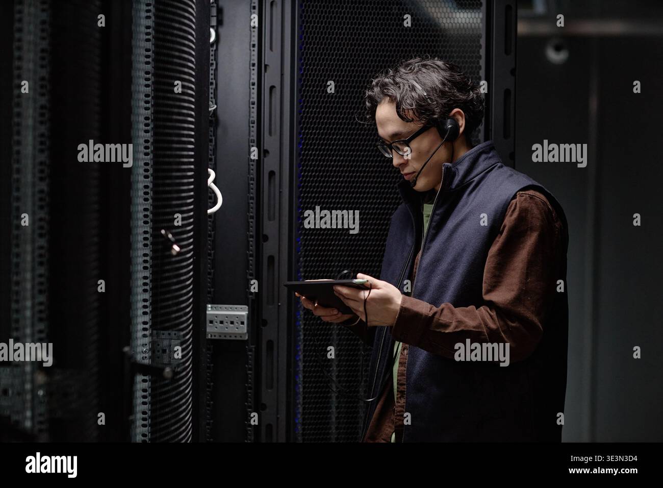 Apparecchiatura server di monitoraggio uomo asiatico giovane adulto che utilizza un tablet digitale Foto Stock