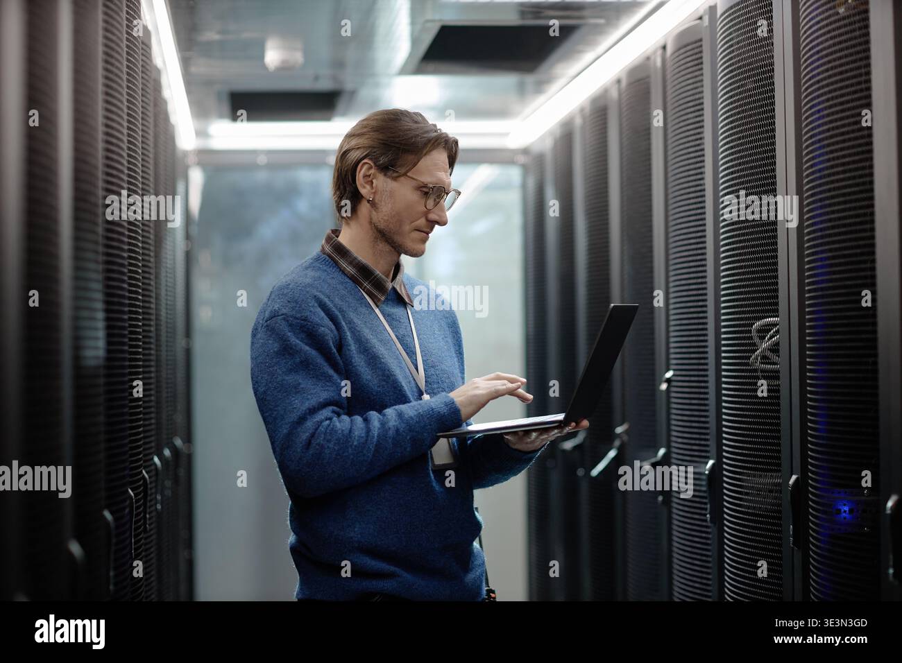 Uomo caucasico adulto che monitora i server dei data center utilizzando un computer portatile Foto Stock