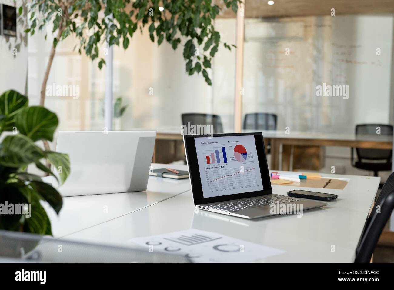 Laptop color argento con carte colorate, appoggiato accanto allo smartphone su una scrivania bianca in un ufficio moderno Foto Stock