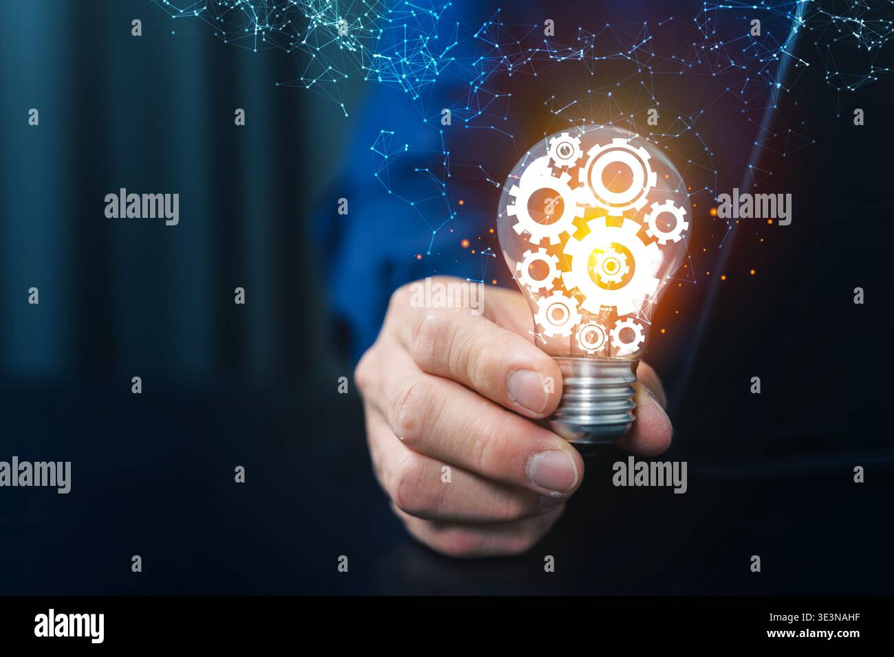Primo piano di una mano che tiene in mano una lampadina luminosa con icone degli ingranaggi e rete digitale vicino a un laptop, simboleggiando l'innovazione, la strategia aziendale, gli automi Foto Stock