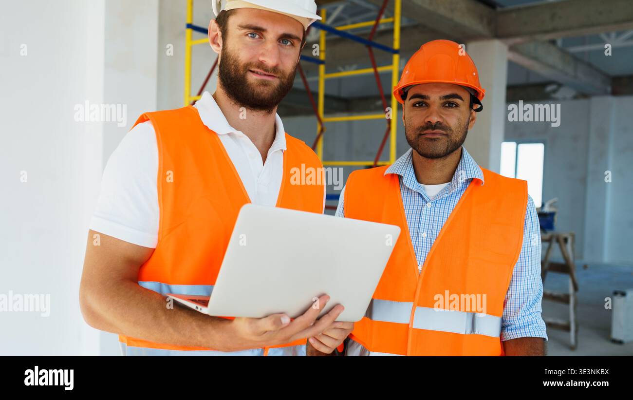 I lavoratori edili controllano i piani su un laptop in un cantiere durante il giorno Foto Stock