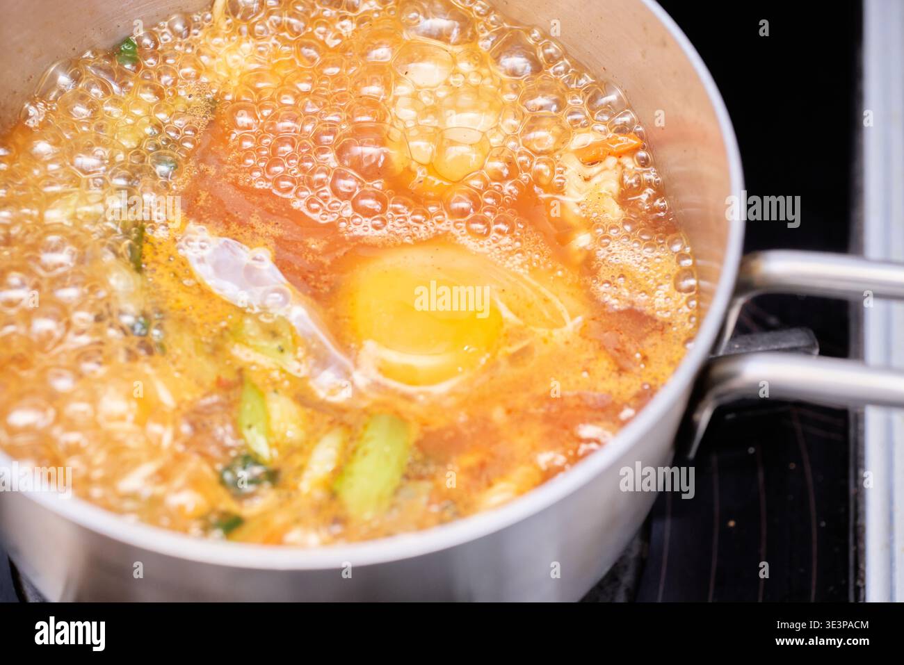 Ramyeon istantaneo coreano piccante bollente con un uovo e cipolle verdi. Il vivace brodo rosso e il vapore promettono un pasto perfetto e accogliente, pronto per il freddo Foto Stock