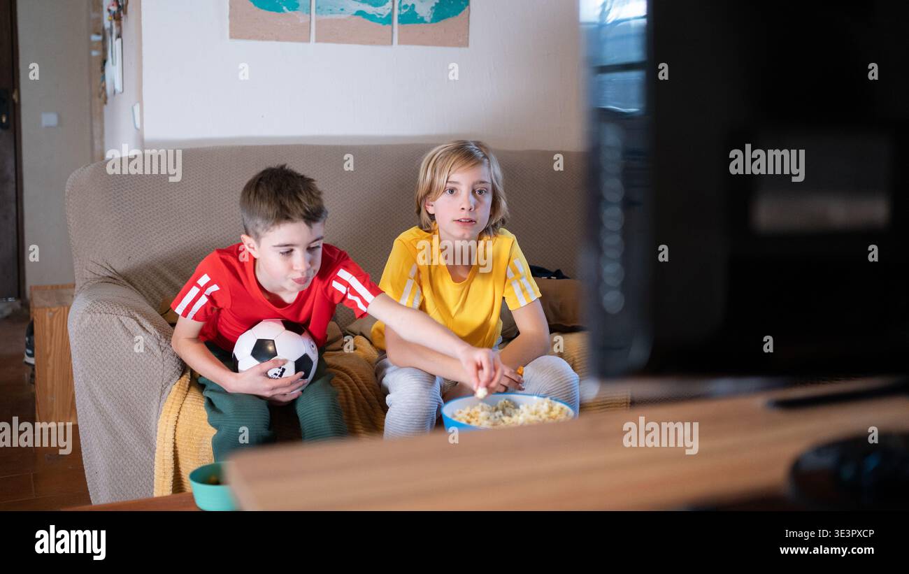 I bambini guardano la partita di calcio in tv mangiando popcorn Foto Stock