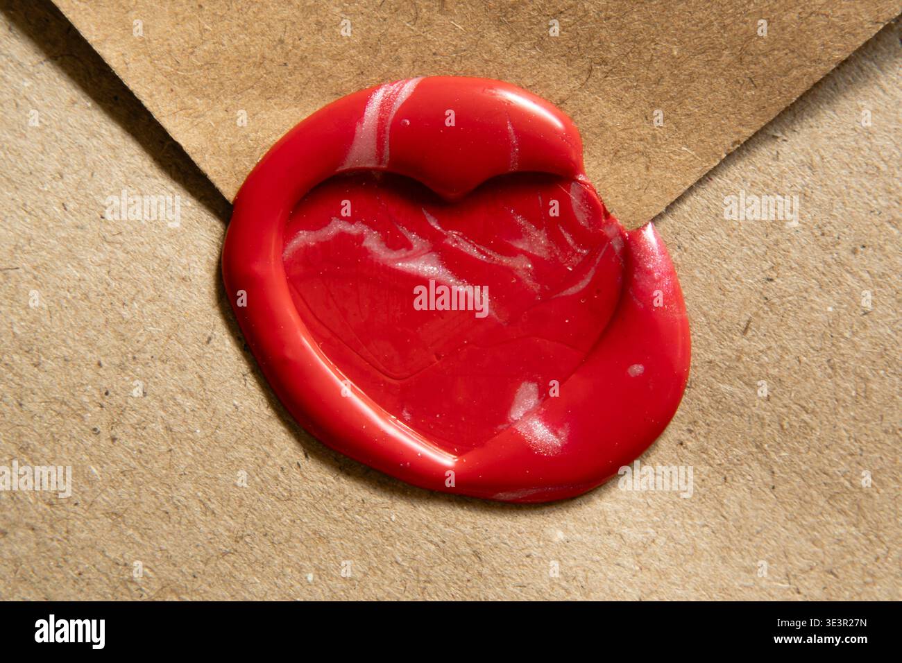 Primo piano di un sigillo di cera rosso brillante con forma a cuore su una busta kraft marrone testurizzato. Lo scatto è caratterizzato da un'illuminazione ad alto contrasto che enfatizza il Foto Stock
